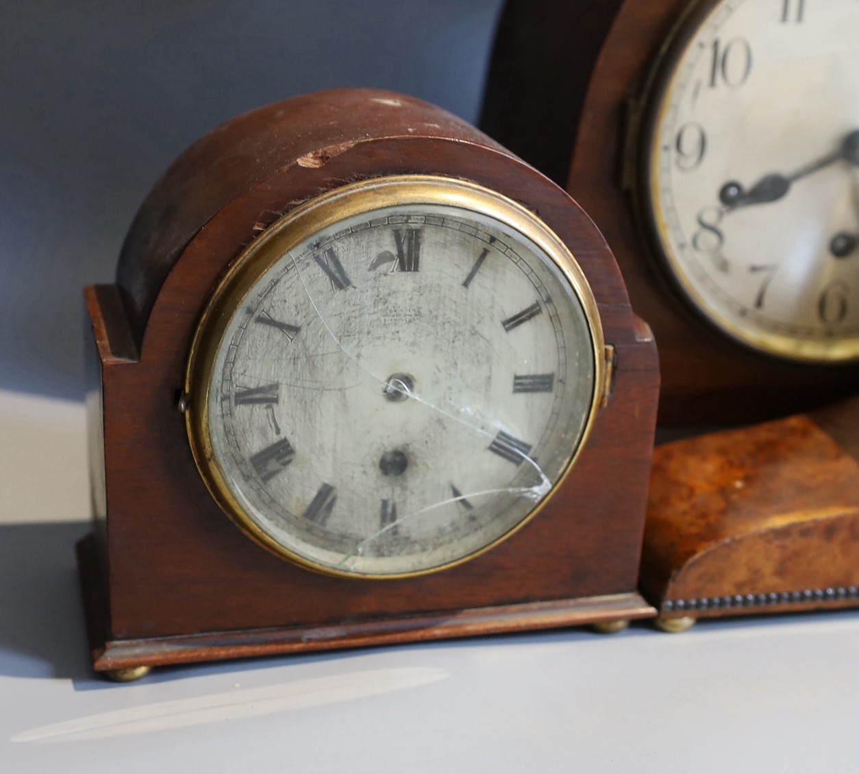 An early 20th century Goldsmiths & Silversmiths amboyna cased mantel clock, width 41cm, together with two other mantel clocks and a wall dial